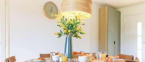 A dining table with breakfast items, a vase with yellow flowers, and a clock on the wall.