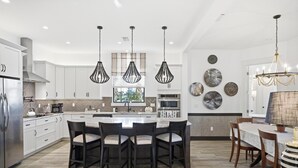 Cocina moderna con armarios blancos, una isla central e iluminación colgante.
