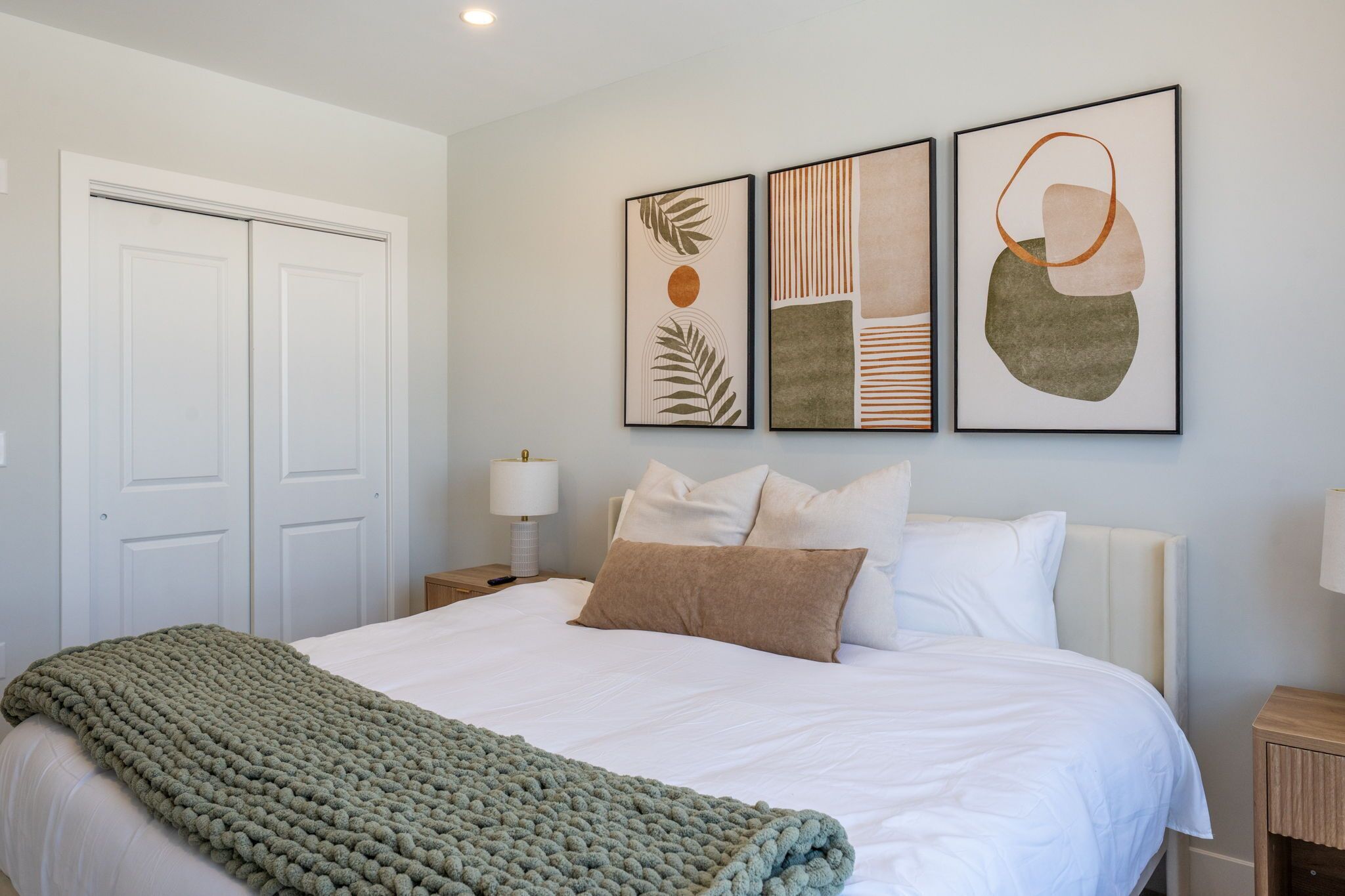 Un dormitorio ordenado con cama, almohadas, una manta y decoración en la pared.