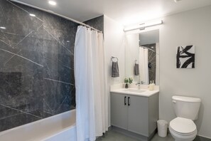 Une salle de bain moderne avec un mur en marbre, une baignoire blanche, un lavabo avec un miroir et des toilettes.