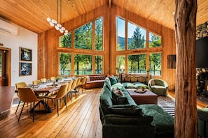 Interior de una cabaña de madera con comedor, asientos y ventanas amplias.