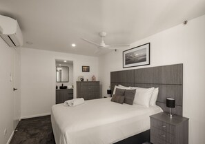 A modern bedroom with a large bed, a bedside table, a wardrobe, a mirror, and a ceiling fan. - Level 26 - Pacific Horizon Retreat (Surfers Paradise)