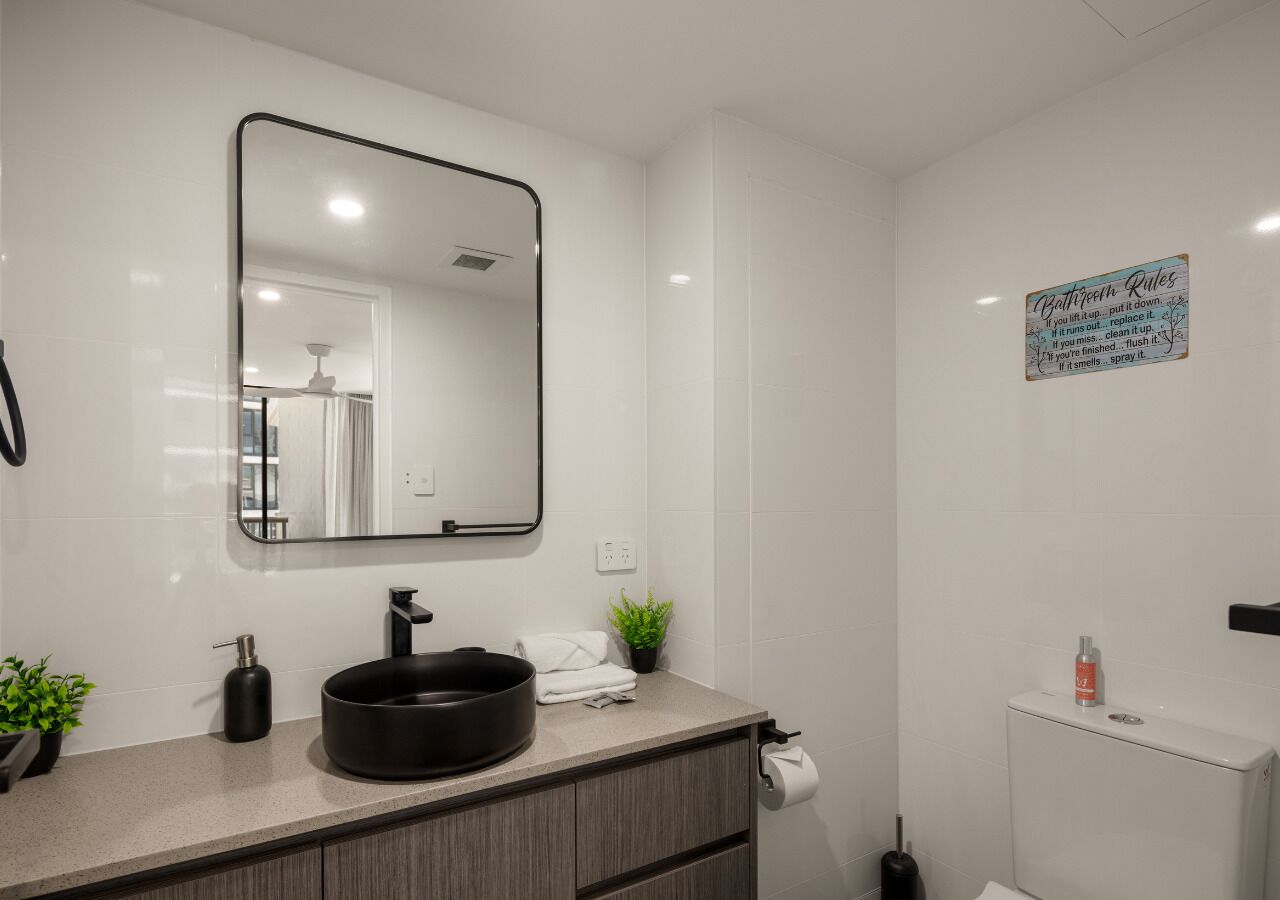 A modern bathroom with a large mirror, a round sink, a toilet, and a small potted plant.
