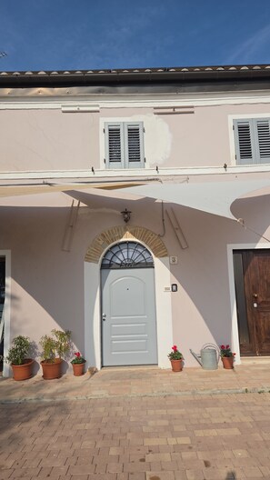 A building with a white door, a small arched window, and a balcony with potted plants. - Old, eco-friendly farmhouse: between the sea and nature (Marche)