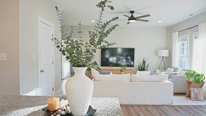 A modern living room with a white sofa, a flat-screen TV, and a ceiling fan. - Cozy Cottage 4BR. in the Heart of Huntersville (Huntersville)