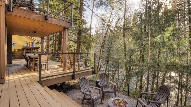 Een terras met houten vloer, een vuurkuil en Adirondack stoelen met uitzicht op een bebost gebied.