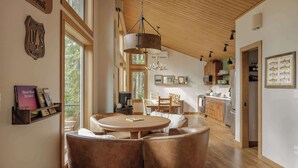 Een ruime woonkamer met een ronde tafel en lederen stoelen, houten balken in het plafond en een keuken op de achtergrond.
