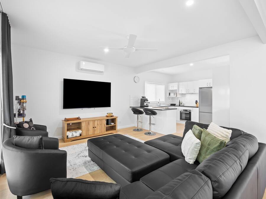 A modern living room with a black sectional sofa, a flat-screen TV, and a wooden entertainment unit.