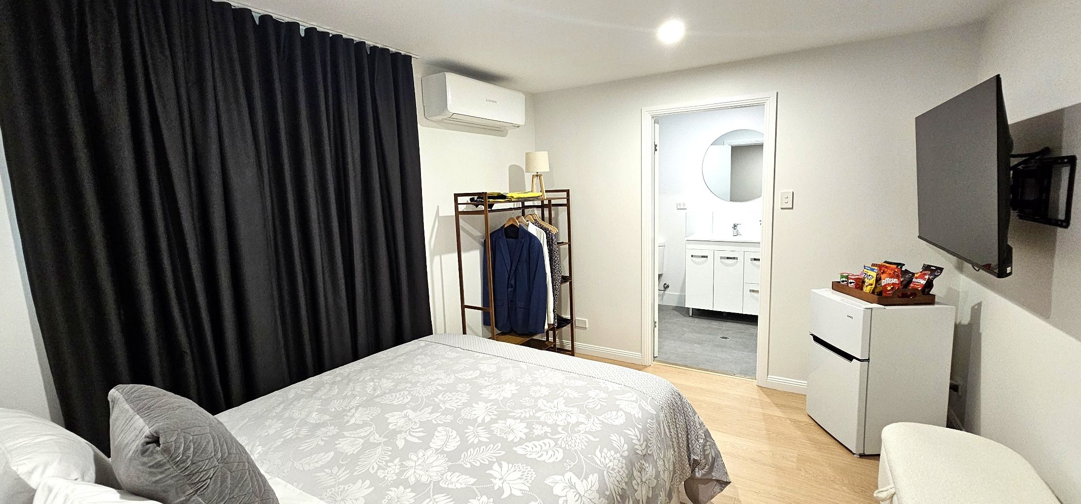 Una habitación de hotel con cama, armario, espejo, televisor y kitchenette.