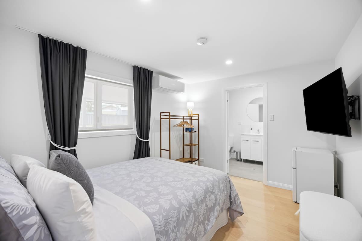 A bedroom with a bed, a wardrobe, a TV, and a bathroom visible through an open door.