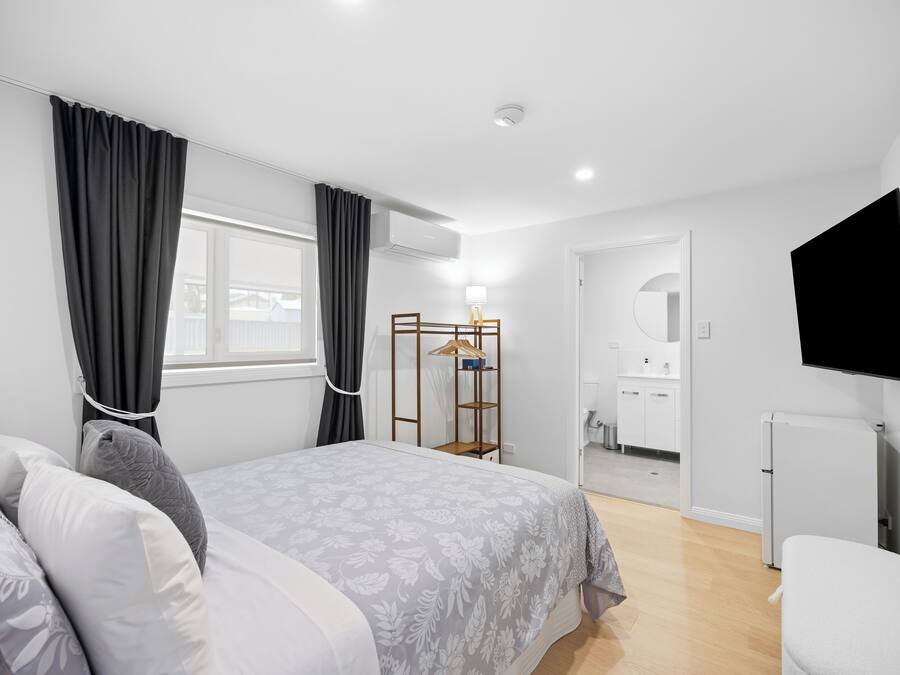 Een slaapkamer met een bed, een kledingkast, een televisie en een zichtbare badkamer door een geopende deur.
