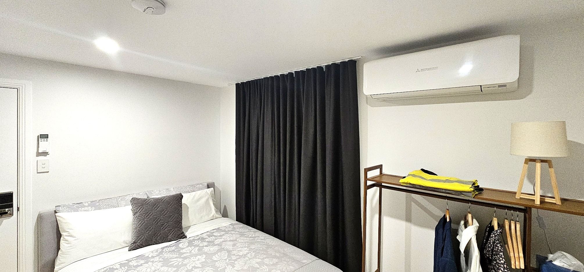 A hotel room with a bed, a wardrobe, a hanging clothes rack, and an air conditioning unit.