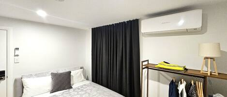 A hotel room with a bed, a wardrobe, a hanging clothes rack, and an air conditioning unit.