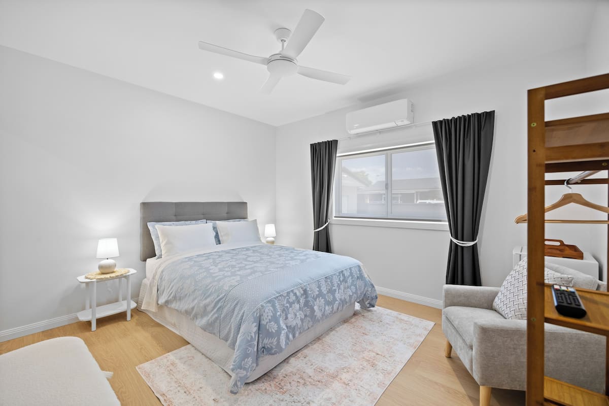 A modern bedroom with a bed, bedside table, nightstand, and a ceiling fan.