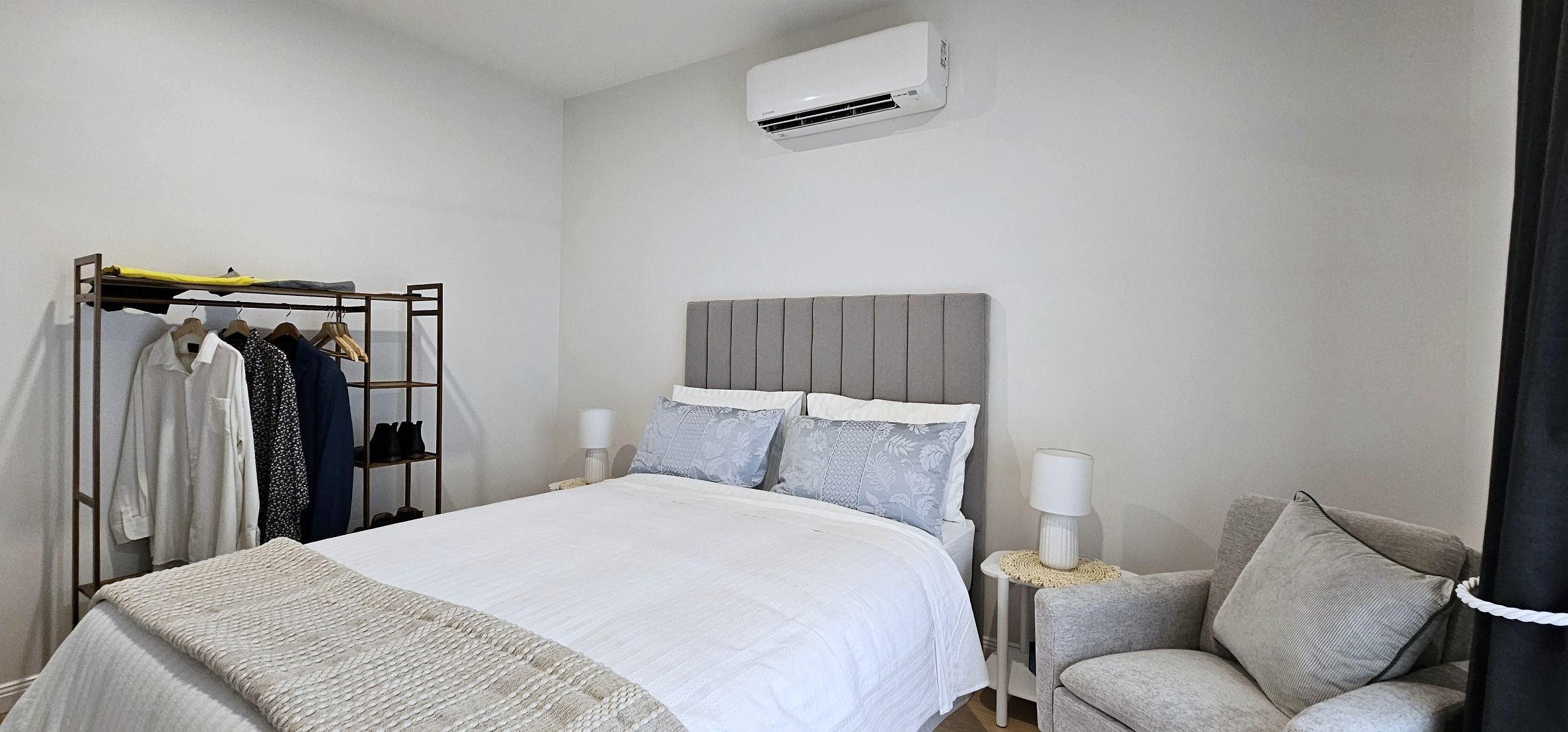 A hotel room with a bed, a wardrobe, a chair, and an air conditioning unit.