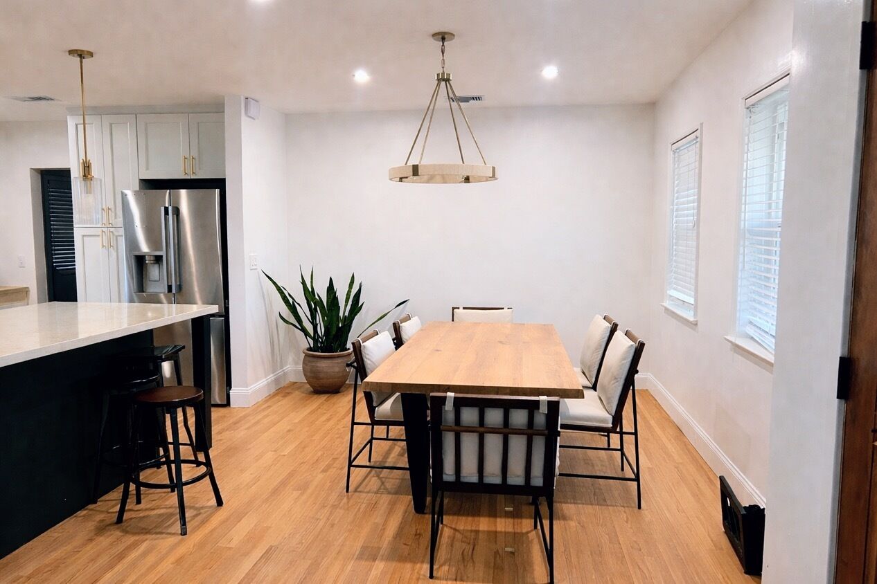 A modern kitchen with a large island, stainless steel appliances, and a wooden dining table with chairs.