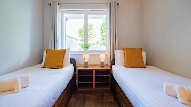 Une chambre double avec deux lits, une petite table avec des lampes, une fenêtre avec des rideaux et une plante sur le rebord de la fenêtre.
