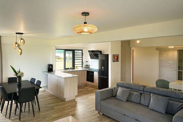 Une cuisine moderne avec un îlot central, un coin repas avec une table et des chaises noires, et un canapé gris dans l’espace salon.