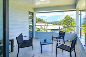 Un balcon avec deux chaises et une table, offrant une vue panoramique sur un paysage verdoyant et des bâtiments.