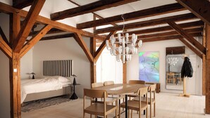 Ruime loft slaapkamer met zichtbare houten balken, een groot bed, een eettafel met stoelen en een kroonluchter.