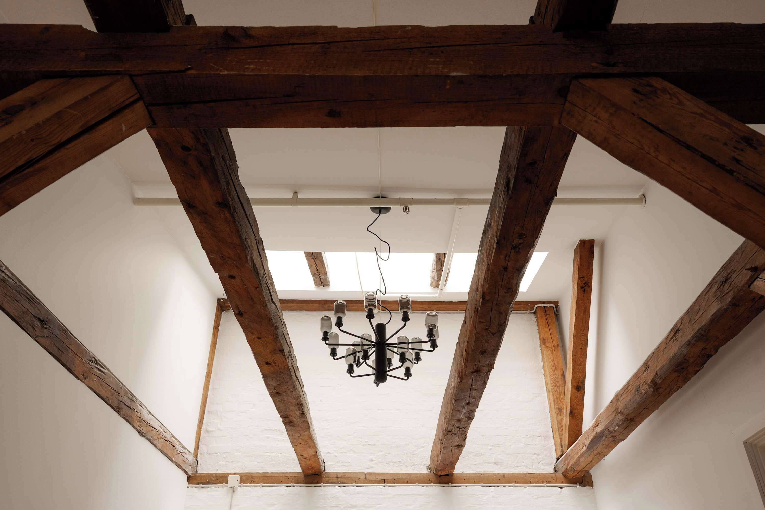 A room with exposed wooden beams, a chandelier, and a white ceiling.