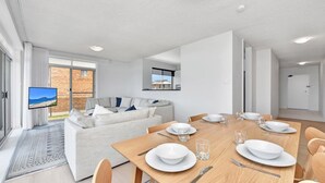 A modern living room with a dining area, a sofa, and a TV. - The Helm 3, 22 Voyager Cl - stunning water views, Wi-Fi (Nelson Bay)