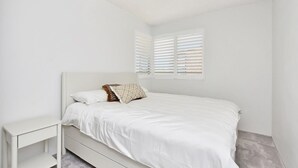 A minimalist bedroom with a single bed, a nightstand, and a window with blinds. - The Helm 3, 22 Voyager Cl - stunning water views, Wi-Fi (Nelson Bay)