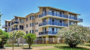 A multi-story residential building with balconies, a fenced yard, and flowering trees. - The Helm 3, 22 Voyager Cl - stunning water views, Wi-Fi (Nelson Bay)