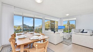 A modern living room with a dining area, large windows, and a view of the outdoors. - The Helm 3, 22 Voyager Cl - stunning water views, Wi-Fi (Nelson Bay)