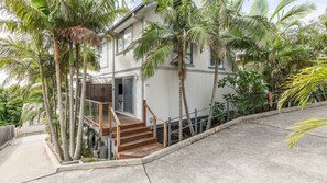 A two-story house with a wooden staircase leading to a balcony, surrounded by palm trees. - Seaview on Government, 58B Government Rd - Water Views, Air Con, Wi-Fi, Linen and Bed Making (Nelson Bay)