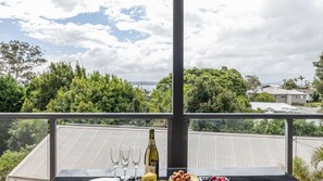 A balcony with a table set for two, featuring a bottle of wine, glasses, cheese, nuts, and fruits. - Seaview on Government, 58B Government Rd - Water Views, Air Con, Wi-Fi (Nelson Bay)