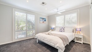 A bedroom with a bed, two bedside lamps, a ceiling fan, and large windows with blinds. - Seaview on Government, 58B Government Rd - Water Views, Air Con, Wi-Fi, Linen and Bed Making (Nelson Bay)
