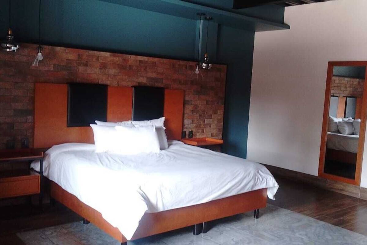 A bedroom with a brick accent wall, a wooden bed frame, and a nightstand with a lamp.