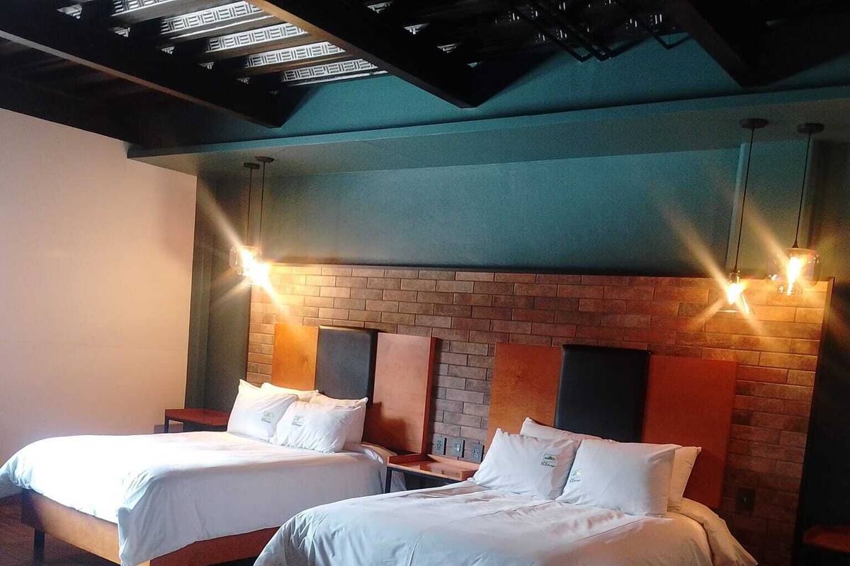 Two twin beds with wooden frames and white bedding in a room with a brick wall and exposed ceiling beams.