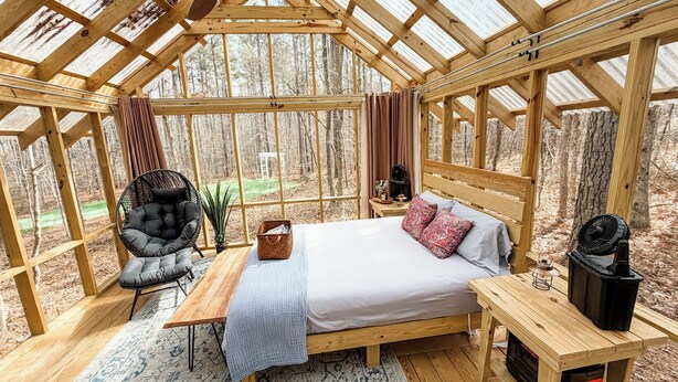 A cozy, wooden-paneled bedroom with a bed, a chair, a table, and a heater.