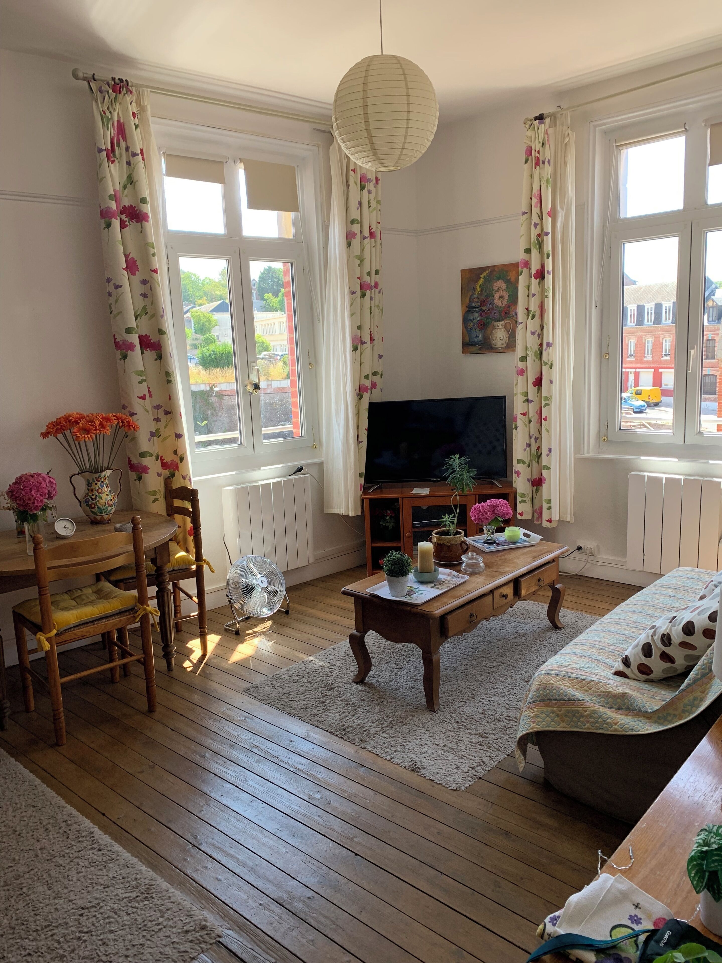 Un salon chaleureux doté d’un parquet, d’un téléviseur à écran plat, d’une table basse en bois et d’un canapé agrémenté d’un coussin à motifs.