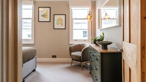 A compact bathroom with a bed, a chair, a dresser, and framed pictures on the wall. - Stunning 2BD Townhouse in Cheltenham (Cheltenham)