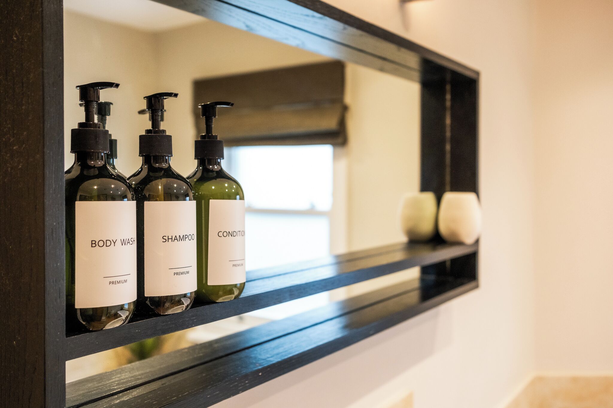 Une étagère de salle de bain avec trois bouteilles de gel douche et de shampoing, ainsi que deux bougies.