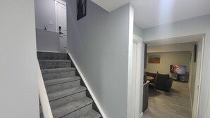 A staircase leading to a living area with a flat-screen TV and a sofa. - Luxurious Home Away From Home With Aircon (Airdrie)