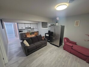 A compact living space with a kitchenette, a sofa, a dining table, and a red chair. - Luxurious Home Away From Home With Aircon (Airdrie)