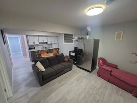 Un espacio habitable pequeño con kitchenette, un sofá, una mesa de comedor y una silla roja.