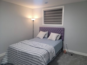 Un dormitorio con cama, mesita de noche, lámpara y aire acondicionado de pared.