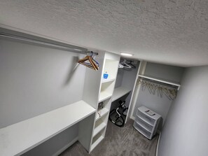 A compact walk-in closet with white shelving, a hanging rack, and a small storage unit.