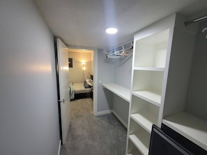 A narrow hallway with a bed, a closet with shelves, and a ceiling light. - Luxurious Home Away From Home With Aircon (Airdrie)