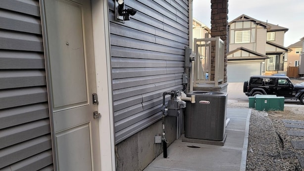 A residential building with a garage door, exterior wall vents, and a parked vehicle. - Luxurious Home Away From Home With Aircon (Airdrie)