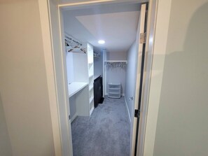 A narrow hallway with a white door at the end, a white closet with shelves and hanging space, and a small white storage unit.