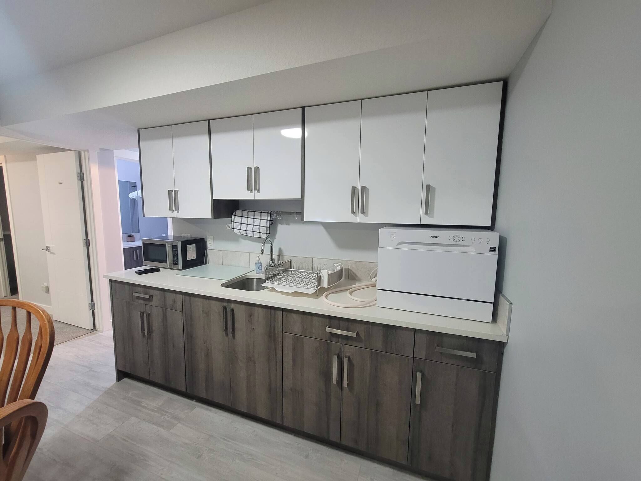 A modern kitchen with white upper cabinets, a built-in microwave, a dishwasher, and a refrigerator.
