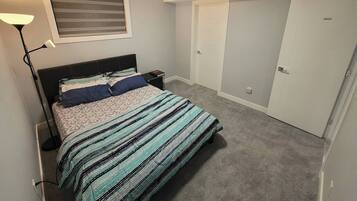 A bedroom with a bed, a nightstand, a lamp, a window with blinds, and a closet.