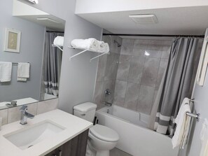 A modern bathroom with a sink, toilet, bathtub, and shower curtain. - Luxurious Home Away From Home With Aircon (Airdrie)