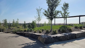 Un área ajardinada con un sendero pavimentado, una colina cubierta de césped y una estructura metálica al fondo.